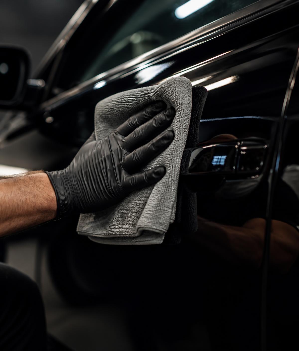 Detailer polishing the door panel of a black car with a microfiber towel